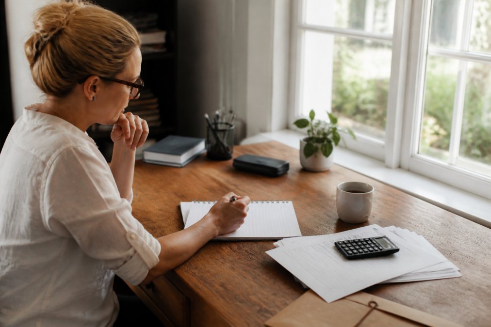 Small business owner at a desk reviewing event management tools on a computer, with calendar, notebook, and coffee visible in a bright home office setting