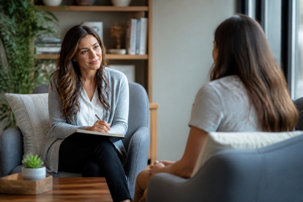 A compassionate therapist in a calm office setting with warm lighting and comfortable seating, listening attentively to an adult patient during a mental health session