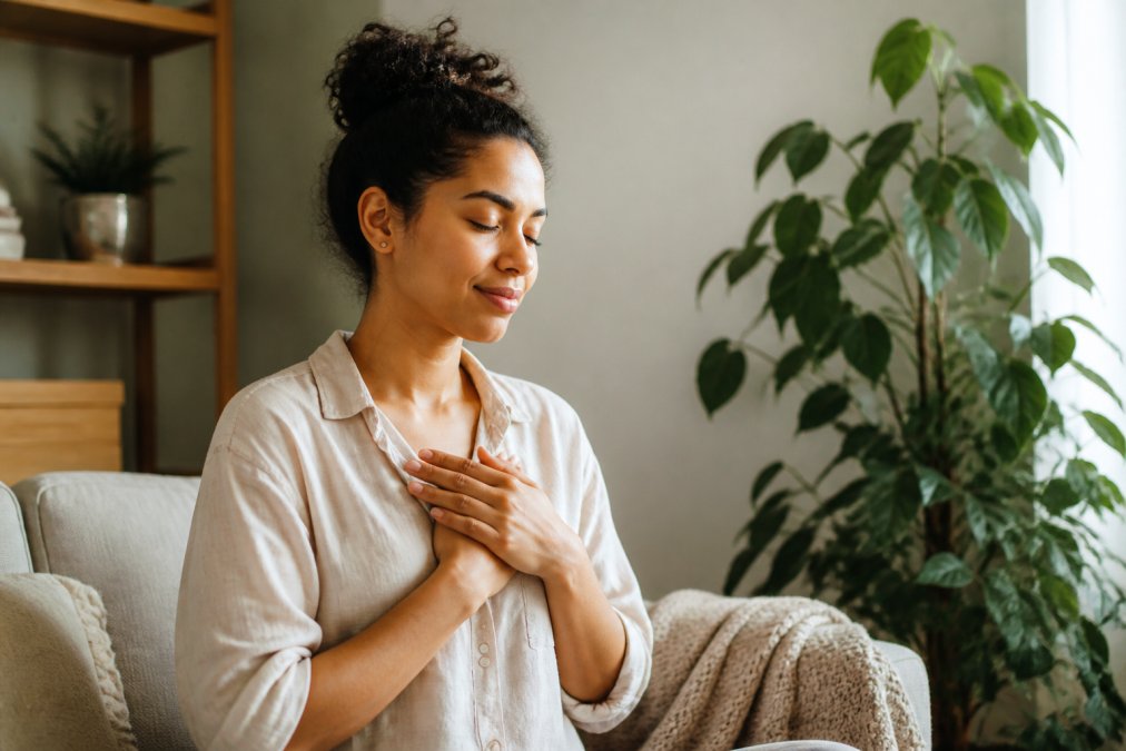 Individual sitting peacefully in a comfortable space, hands on chest in a self-soothing gesture, with a thoughtful, accepting expression