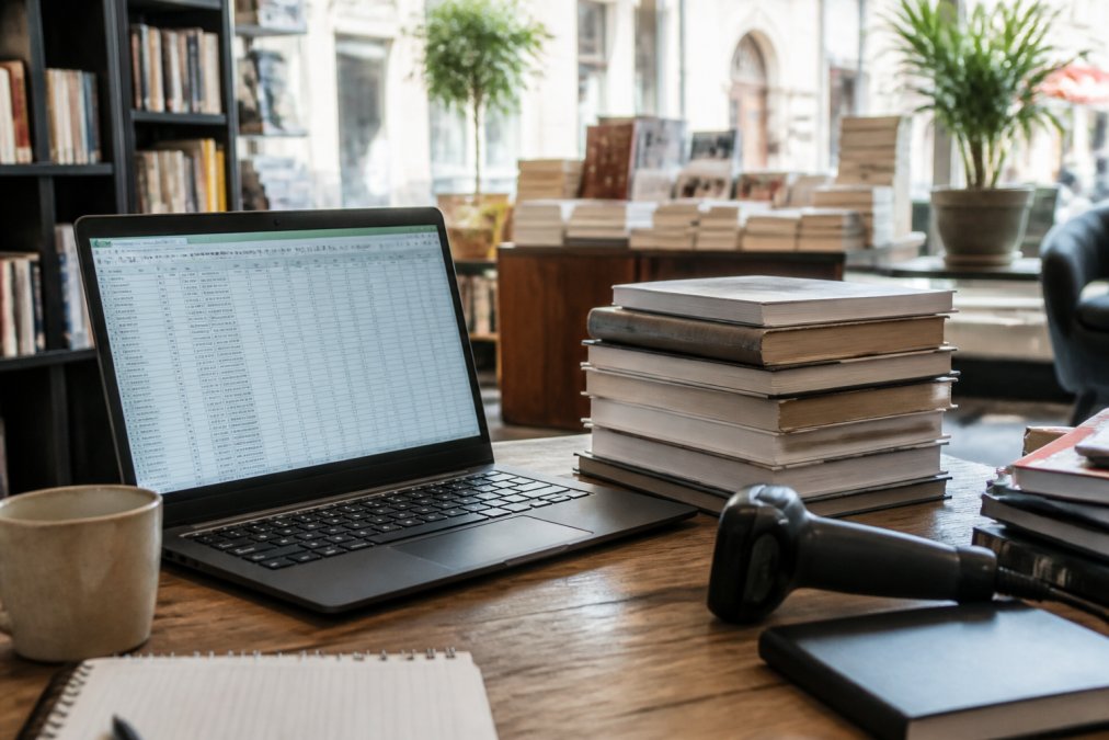 Scrivania di una libreria con portatile, lettore di codici a barre e libri per gestire l'inventario libri del negozio.
