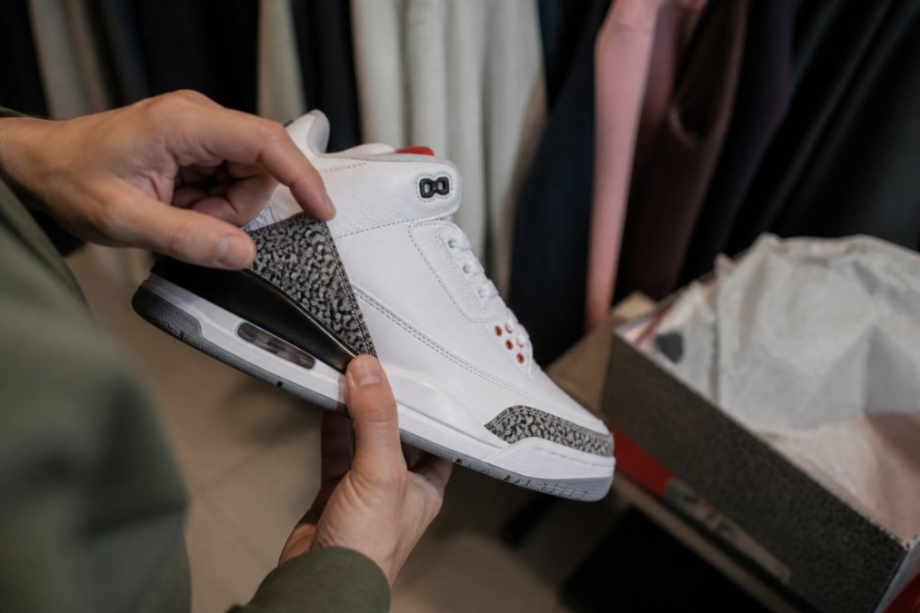 Close-up van handen die details van een sneaker inspecteren: nauwkeurigheid van stitching, logodetails, materialen en zoolconstuctie