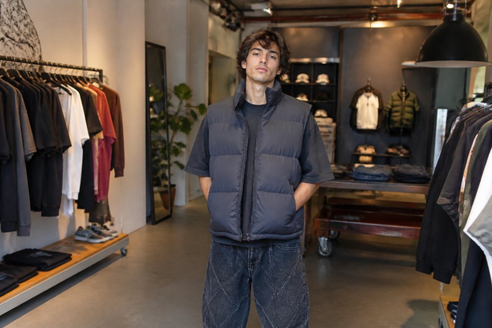 Modebewuste jongvolwassene in trendy oversized streetwear outfit staat in een moderne, goed verlichte winkel met vintage en contemporary kleding displays, zelfverzekerde houding terwijl ze naar camera kijkt