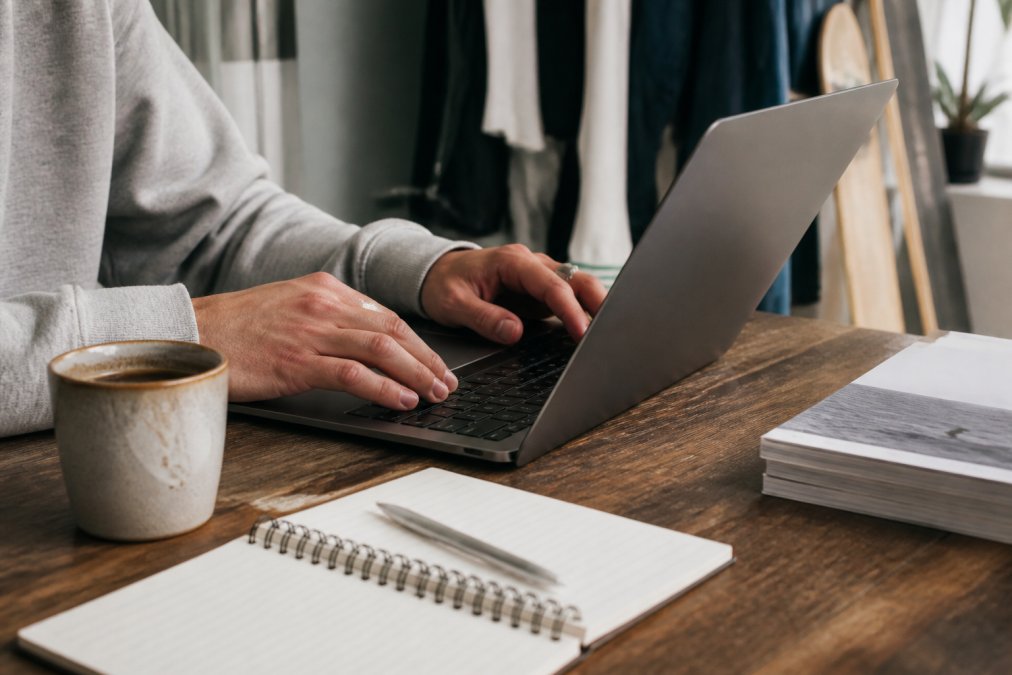Iemand die op een laptop zoekt naar exclusieve streetwear online kopen met een koffiekopje en notitieblok op het bureau.