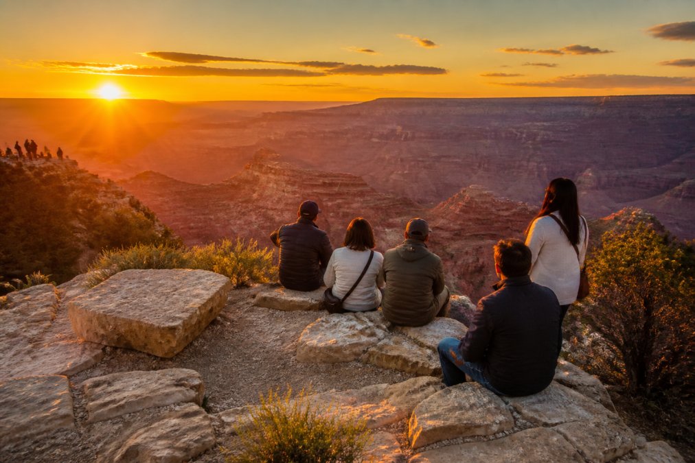 Golden hour light illuminating the canyon rim with visitors silhouetted against layered geological formations and warm amber sky