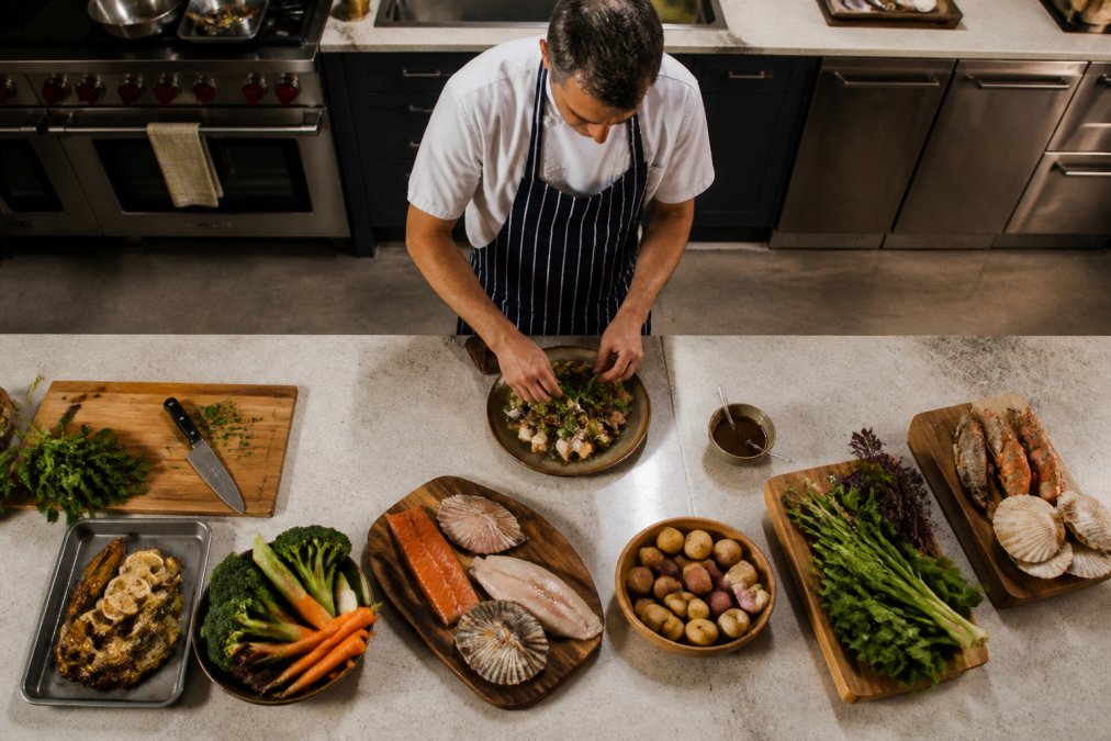 An overhead view of a gourmet meal being prepared in a modern Highland lodge kitchen, with locally sourced ingredients on the counter and professional cooking equipment