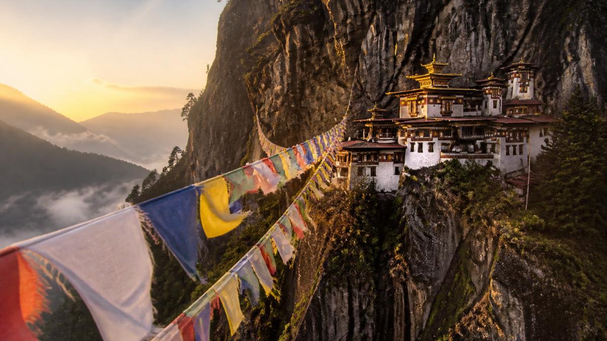 Golden-roofed monastery perched on a misty mountainside at dawn, prayer flags fluttering in wind, forested valleys visible below in soft morning light