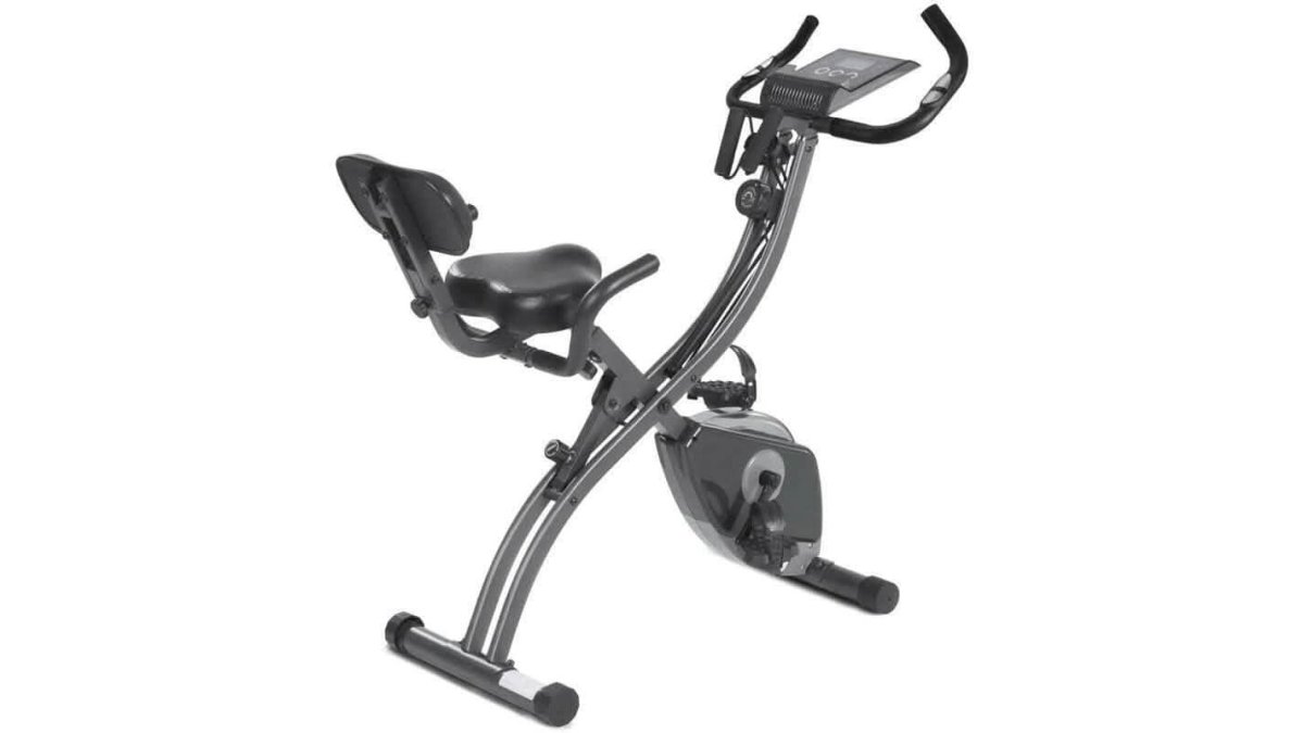 Folding stationary bike in a compact apartment corner, partially folded, with resistance bands visible, next to a window