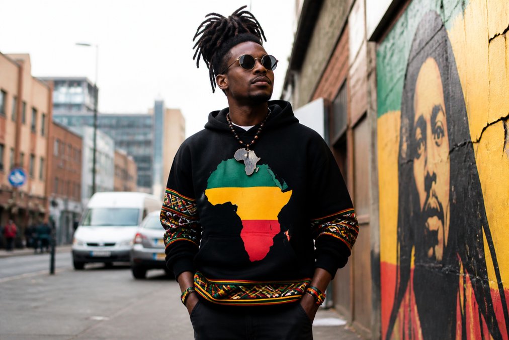 Person wearing reggae-inspired conscious streetwear with Pan-African graphics, standing confidently in an urban setting, showing how cultural expression translates through intentional fashion choices