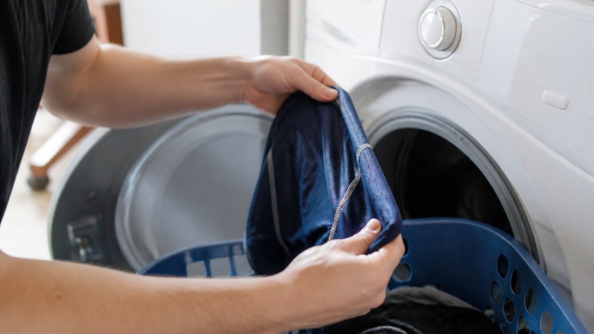 Close-up of someone turning a moisture-wicking athletic shirt inside out before placing it in a washing machine with cold-water setting visible on the dial