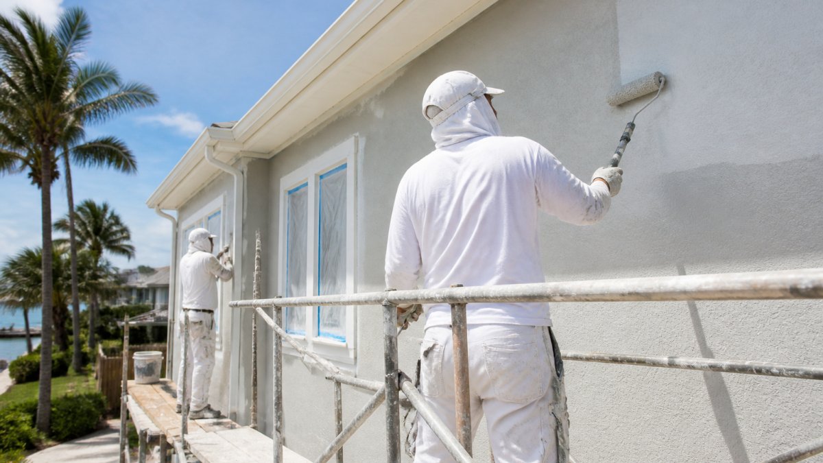 Painting crew applying gray coating to a coastal stucco home to manage exterior house painting cost Florida.