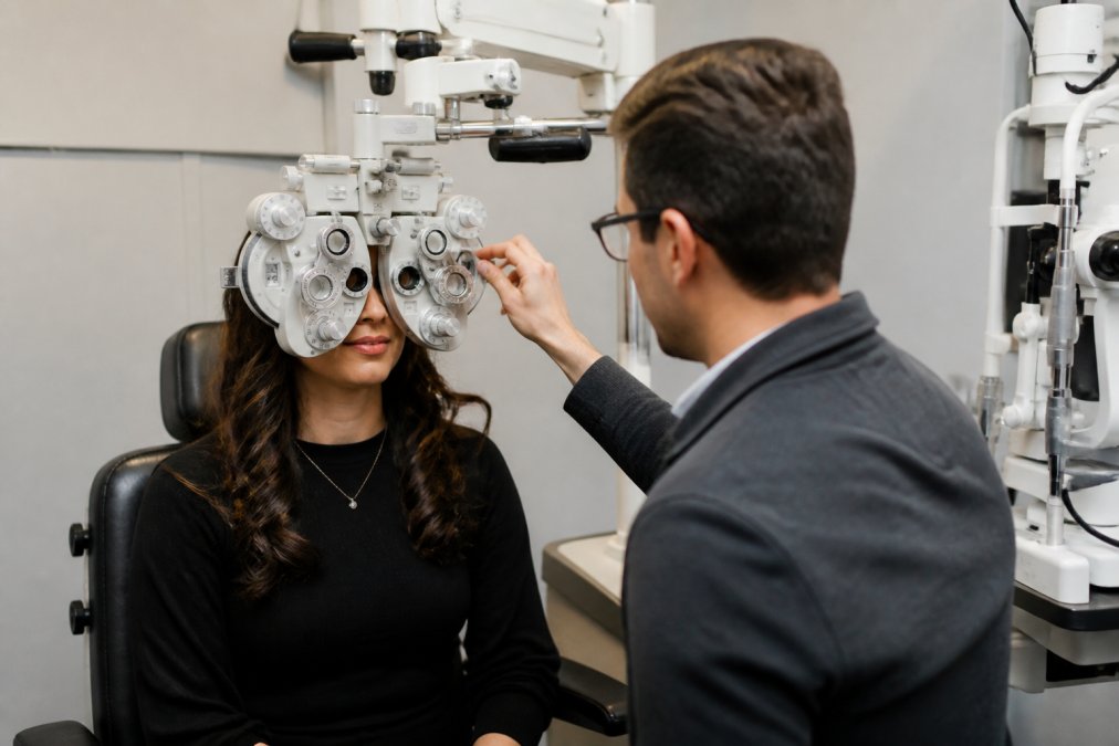 Patient sitting in a modern optometry office during an eye exam with advanced diagnostic equipment visible in the background