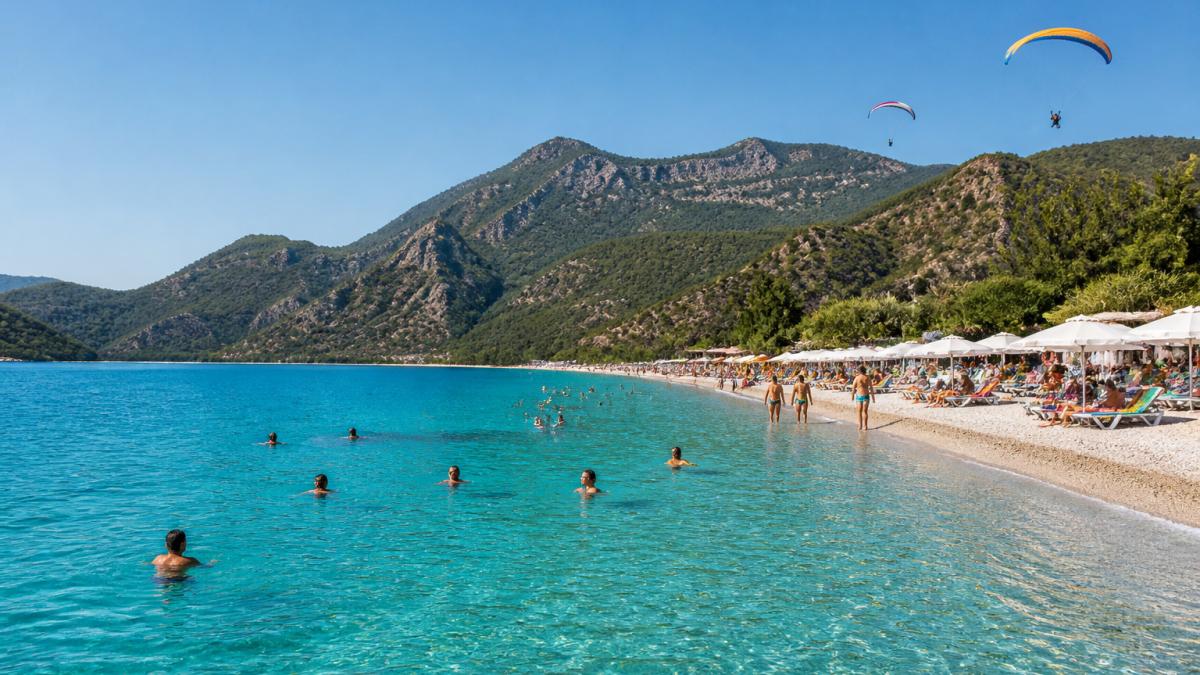 Turkuaz denizde yüzen insanlar, güneşli eylül gününde Fethiye plajının kumsal ve arka planda yamaç paraşütü sporcuları görülüyor