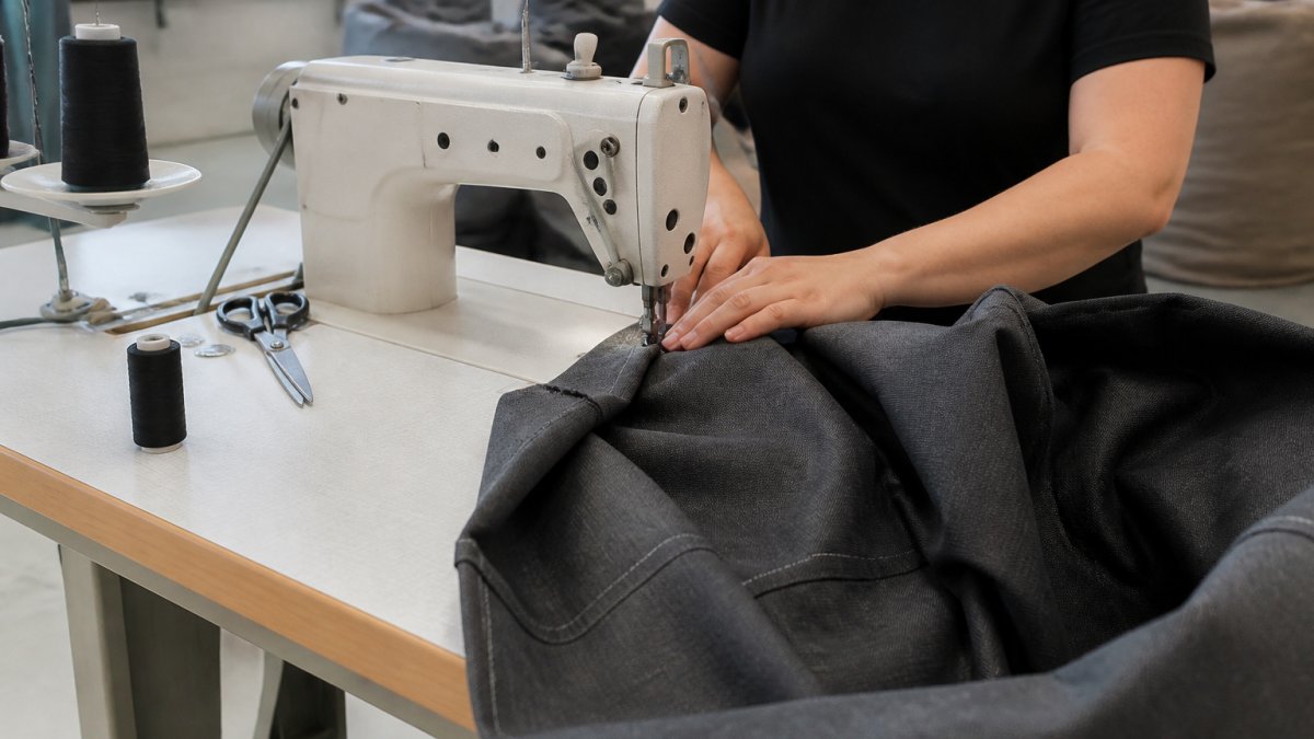 Mains assemblant et cousant les panneaux de tissu d'une housse de pouf géant à la machine dans un atelier.