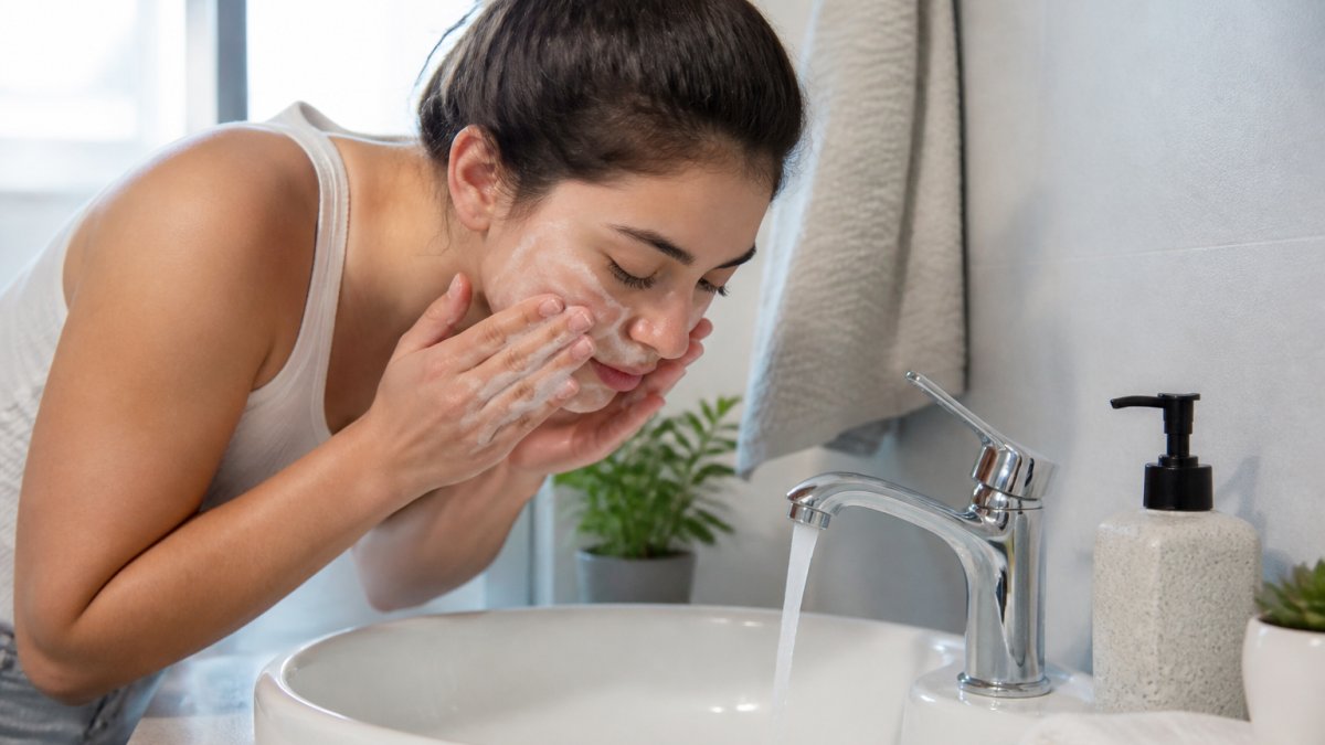 Person gently massaging face with a gel cleanser at bathroom sink with lukewarm water and soft lighting