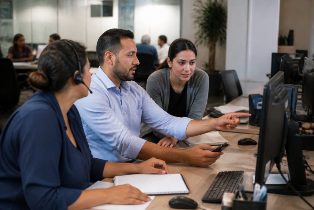 Team of home service dispatchers collaborating in an office, looking at computer monitors displaying automated workflow status and lead assignments
