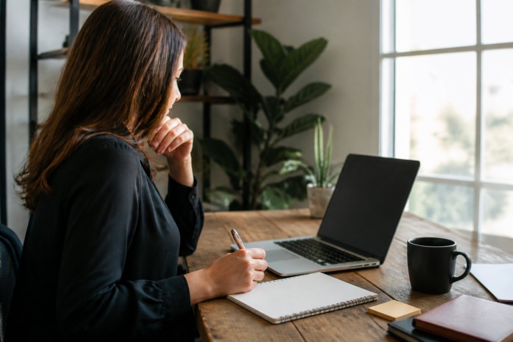 Professional woman reviewing analytics on a laptop screen with a notepad and growth charts visible, representing income tracking and business expansion in natural office lighting