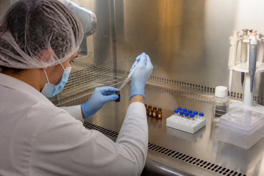 Laboratory technician carefully transferring peptide solution into amber vials for storage, using sterile technique with gloved hands under a biosafety hood with controlled lighting