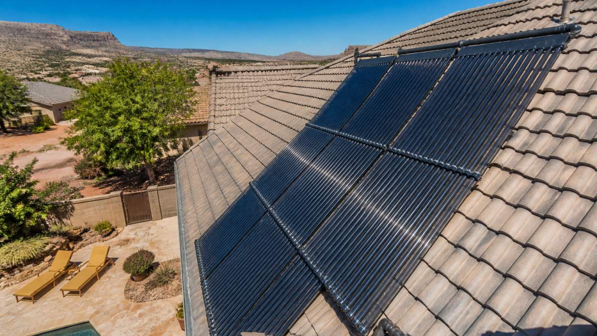 Overhead view of solar pool heater panels mounted on a residential roof with clear blue sky and direct sunlight, showing the collector array installed on a pool deck