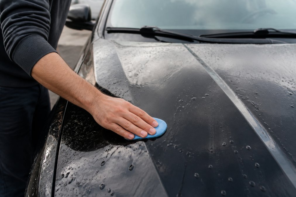 Close-up of a person using a clay bar on a freshly washed car's paint surface, with water beads visible, demonstrating pre-appraisal detailing