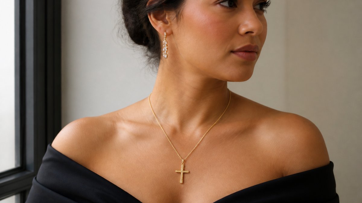 Woman in formal black-tie attire wearing an elegant gold cross necklace, photographed from shoulders up with natural lighting against a neutral background