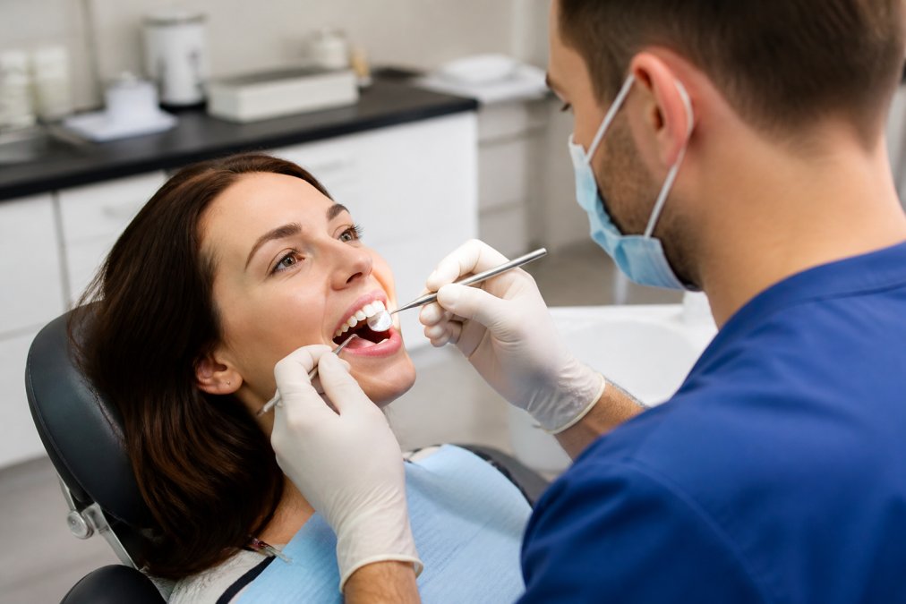 A patient smiling in a dental chair while the dentist examines their teeth with professional lighting in a modern treatment room