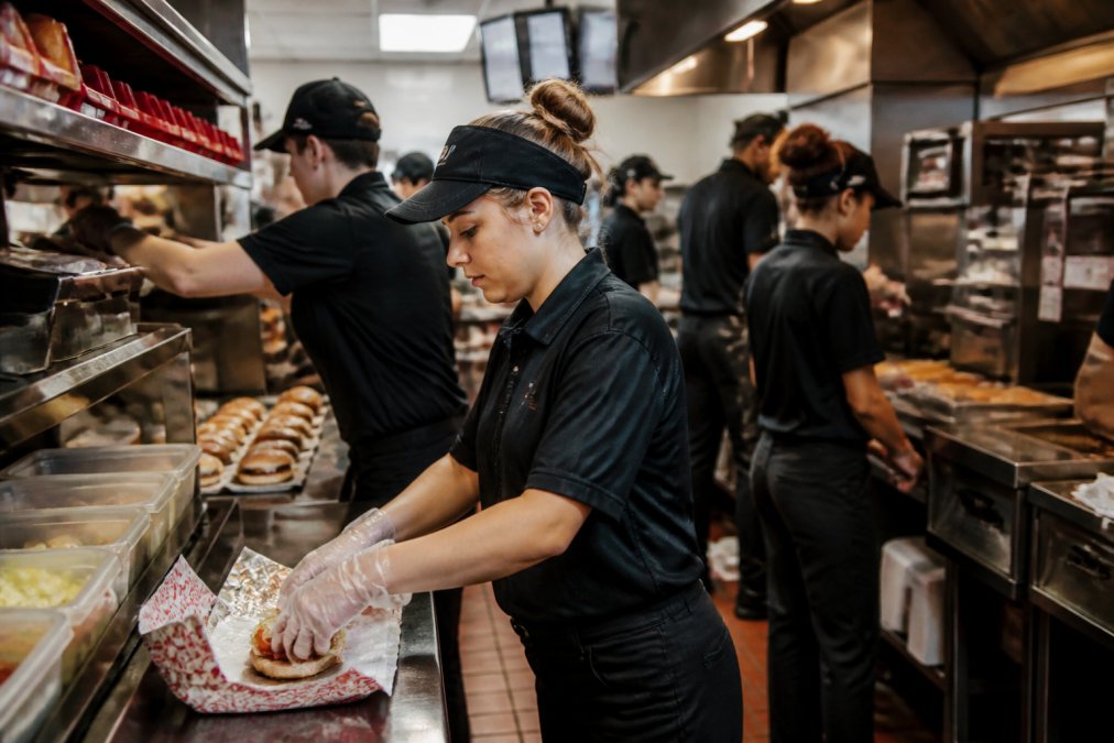 Staff managing a digital ordering system in a busy kitchen during peak fast food operating models service hours
