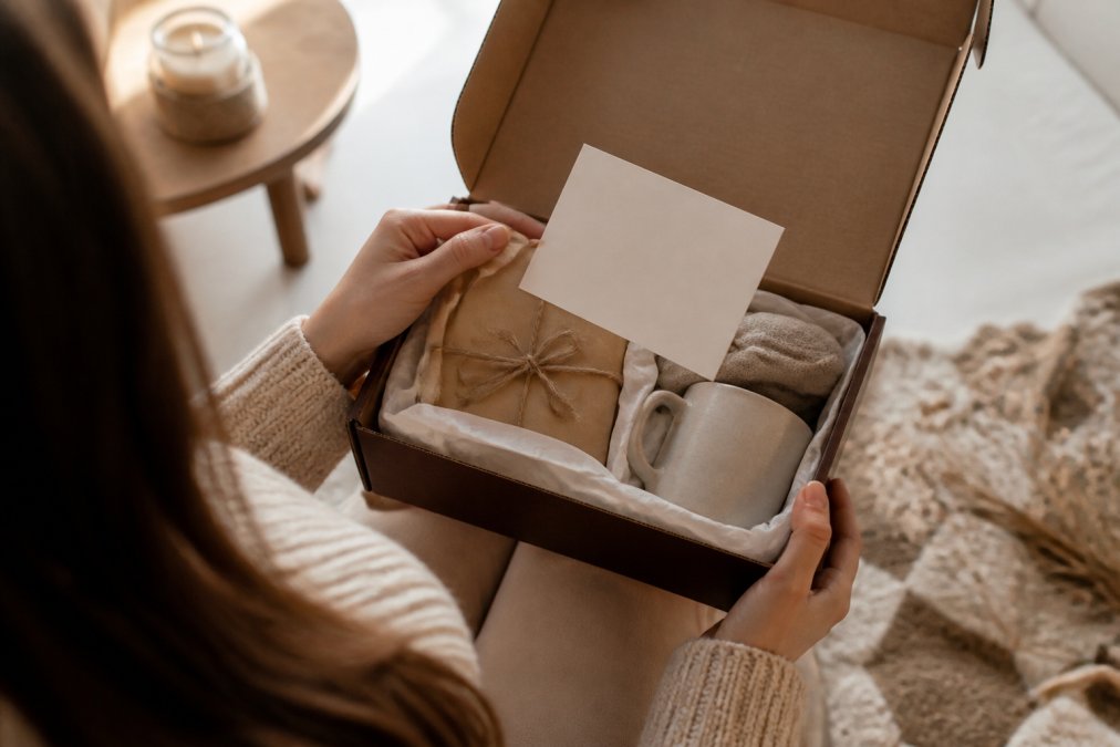 Hands holding open a personalized gift box with tissue paper and handwritten note card, showing the unboxing experience of a custom keepsake with soft natural lighting