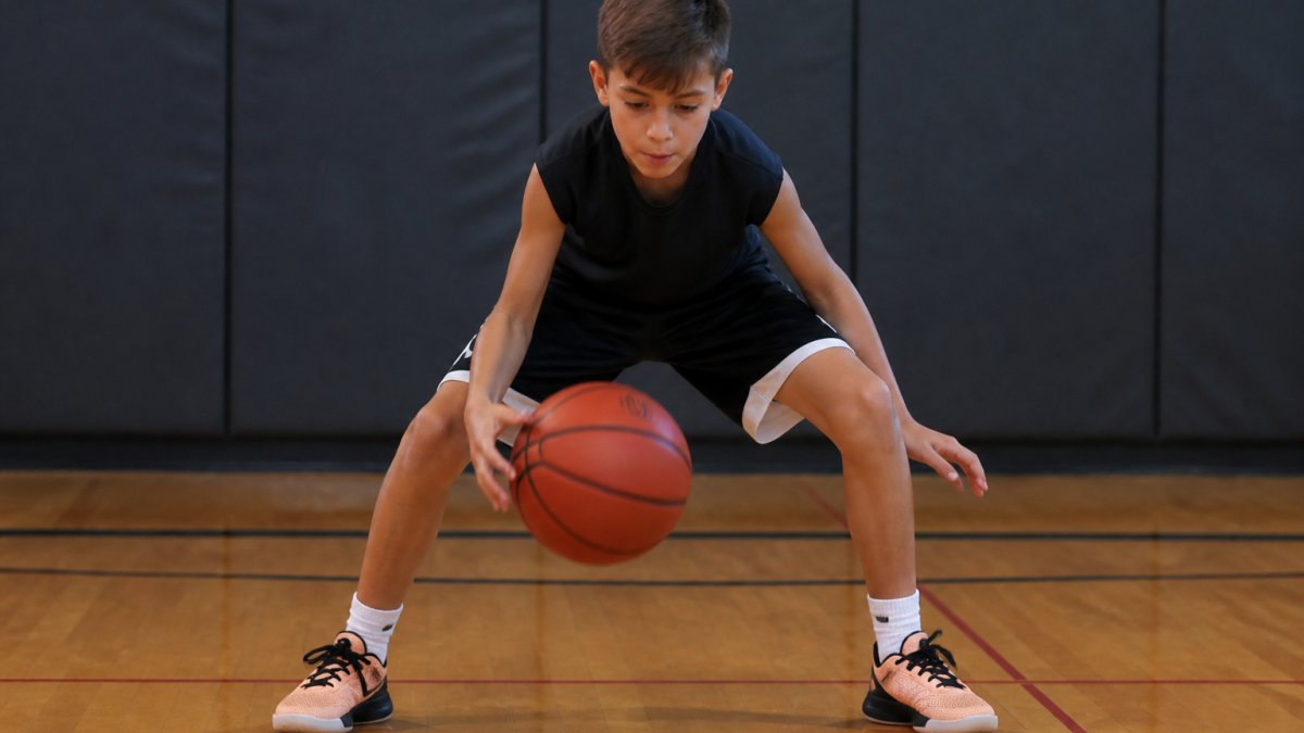 Youth basketball player in a low stance practicing a faster crossover youth move on an indoor court