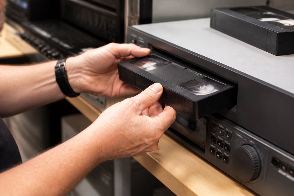 Professional hands carefully inserting a VHS tape into high-end digitisation equipment in a clean, well-lit studio environment with precision care