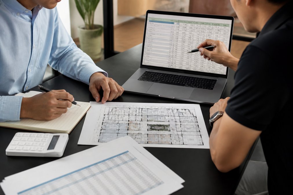 Business owner and consultant reviewing an FEC startup budget on a laptop with a floor plan nearby.