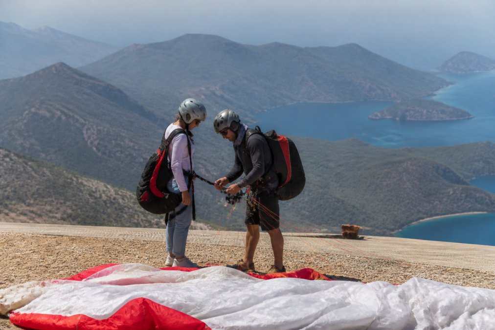 Turist ve pilot Babadağ tepesinde kalkış öncesi paraşüt ekipmanını kontrol ederken, geniş açıdan manzara ve dağ peyzajı