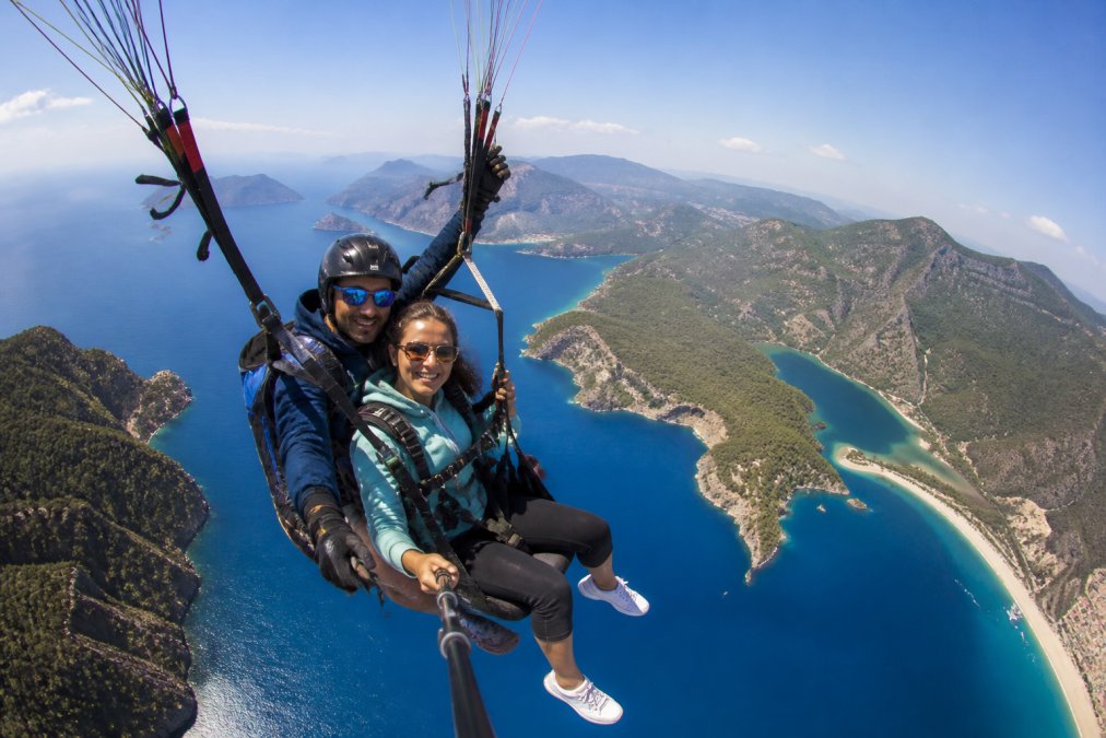 Paraglider pilot ve turist tandem uçuş sırasında gökyüzünde, arka planda Ölüdeniz'in turkuaz denizi ve Fethiye kıyı şeridi