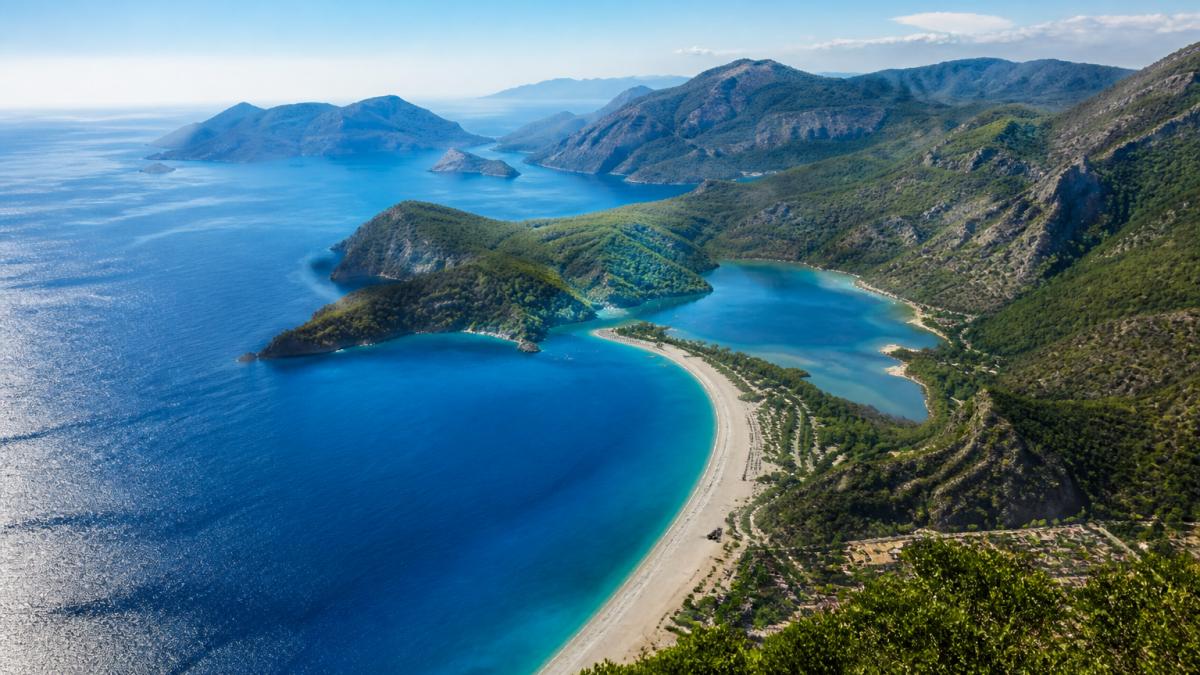 Fethiye'nin sahil çizgisinin kuş bakışı görünüşü, turkuaz suları ve beyaz kumlu plajlar, arka planda dağlar ve yeşil ormanlar
