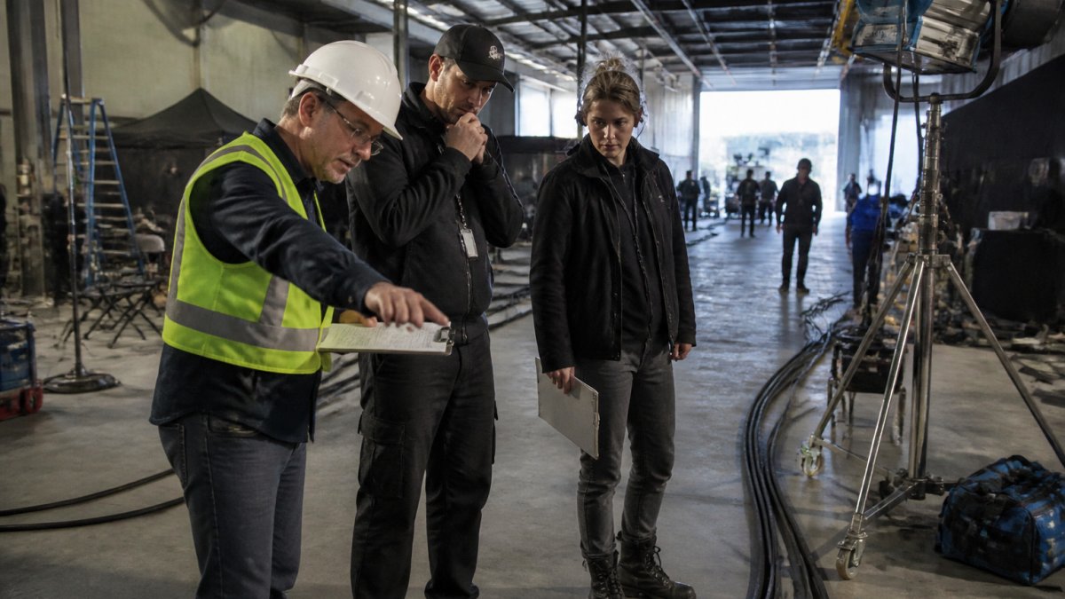 Film production safety compliance officer reviewing hazardous cable runs with crew members on a busy set