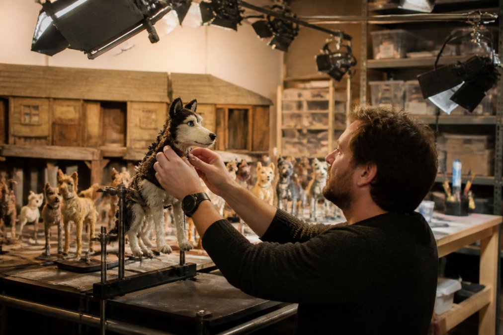 Stop-motion animation studio workspace with puppet rigs mounted on adjustable armatures, professional lighting rigs positioned overhead, detailed miniature set construction in background, animator's hands adjusting a puppet figure mid-frame