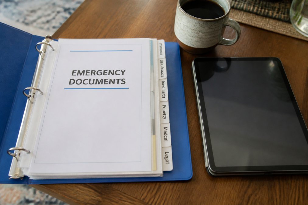 Close-up of an organized emergency binder with labeled tabs and documents, alongside a tablet displaying digital files, representing both physical and digital document storage