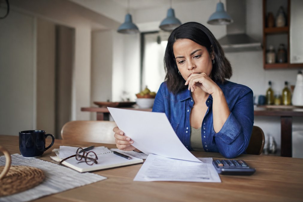 A person reviewing financing paperwork at a kitchen table with a laptop and calculator, looking thoughtful