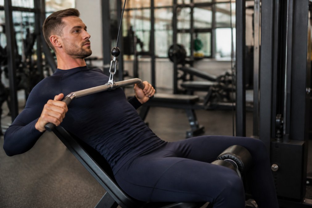 Person wearing well-fitted compression activewear during intense gym workout, demonstrating proper support across shoulders and torso with full range of motion visible