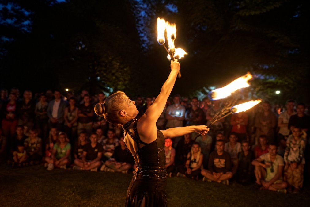 Professionel ildartist udfører spektakulært ildshow udendørs om aftenen, med orange og gule flammer der lyser op i mørket foran et begejstret publikum på en byfest