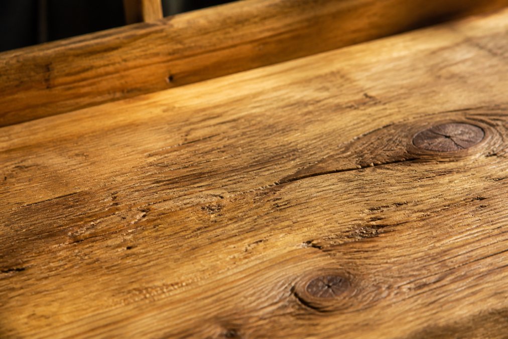 Close-up of aged solid wood grain showing natural patina and character marks from years of use, with weathered surface texture and warm honey tones in natural sunlight