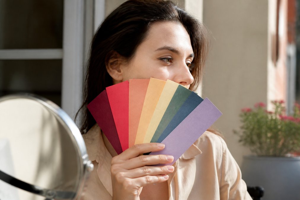 Person holding color swatches up to their face in natural daylight, examining how different hues and tones complement their complexion