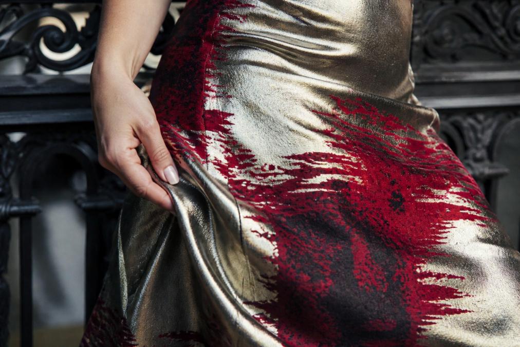 Close-up of a woman's hand gently touching the flowing fabric of an elegant evening gown, showing the delicate drape and texture of breathable material catching natural light
