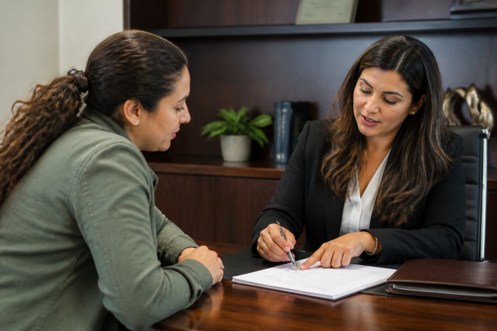 Customer and Spanish-speaking insurance professional having conversation at desk, agent pointing to details on policy document with professional warmth