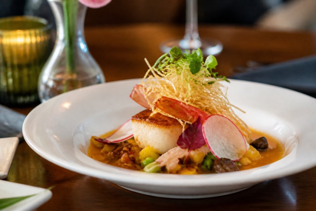 Beautifully plated Asian fusion dish featuring fresh local seafood with vibrant garnishes and artistic presentation on white porcelain in elegant fine dining setting