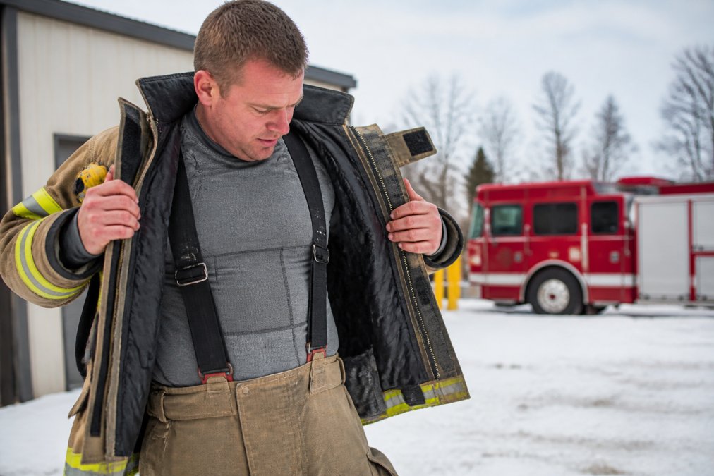 Professional firefighter in full cold weather training gear demonstrating proper layering system with visible base layer, insulation, and fire-resistant outer shell during outdoor winter training exercise in snowy conditions