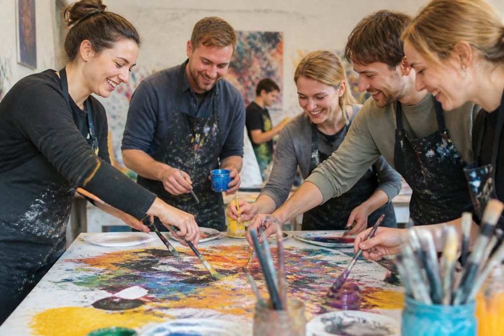 Gruppe von Mitarbeitern in einem kreativen Workshop, gemeinsam an bunten Kunstprojekten arbeitend, mit Farben und Materialien, fröhliche Atmosphäre