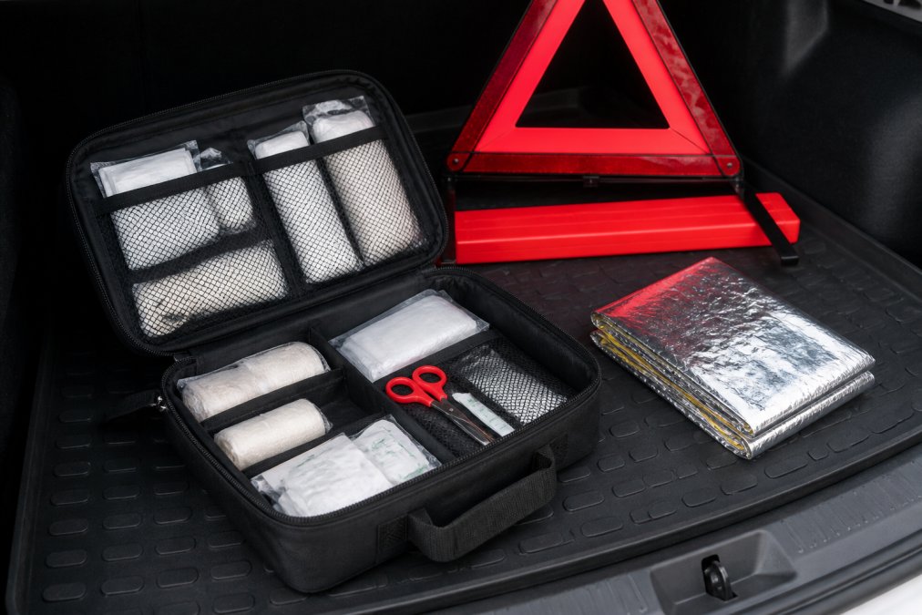 Diagram of a first aid box showing organized medical supplies, emergency blanket, and reflective triangle for cars.