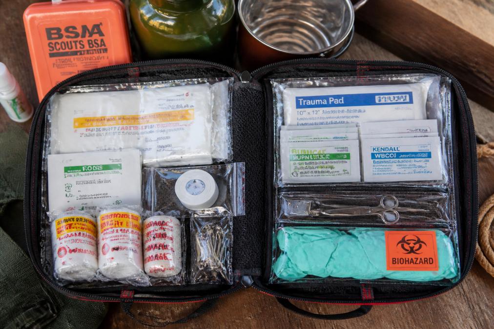 Close-up of first aid kit contents including gauze pads, adhesive bandages, antiseptic wipes, medical gloves, and blister care supplies laid out in organized waterproof compartments