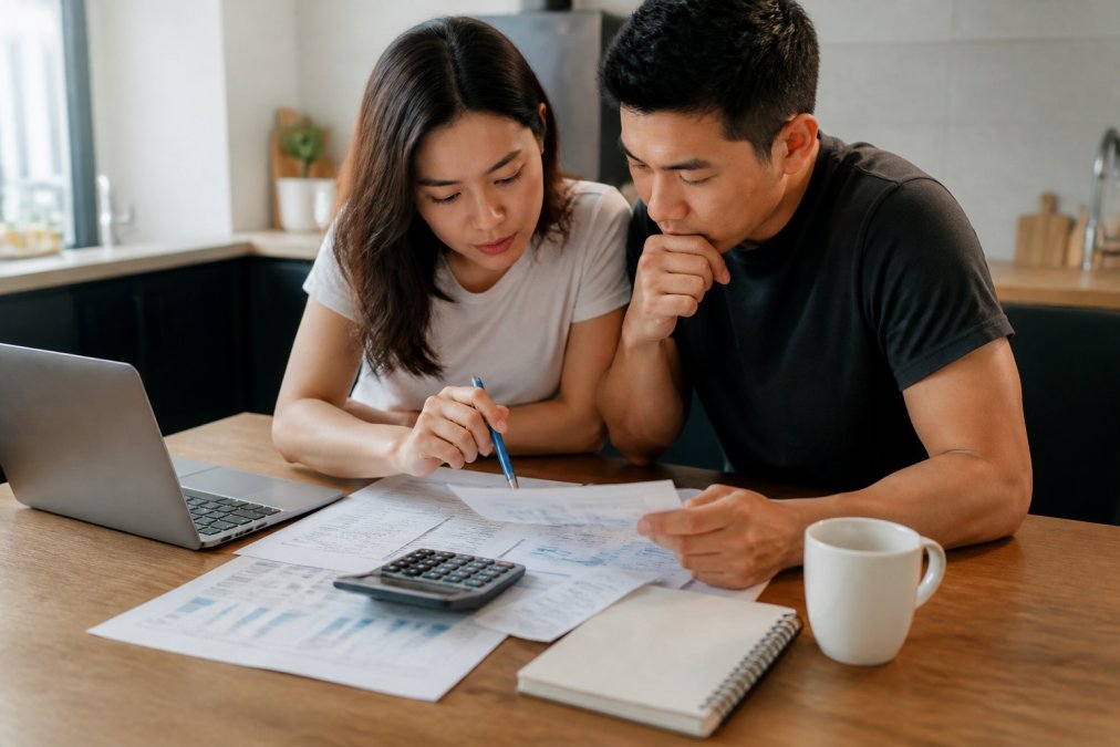 A young couple reviewing financial documents and a mortgage calculator on a laptop at a bright kitchen table with a cup of coffee