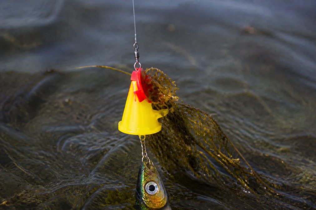 Close-up of Fishing Weed Blocker device attached to fishing line with lure, showing the guard mechanism in action as it moves through water with vegetation, photographed in natural outdoor lighting